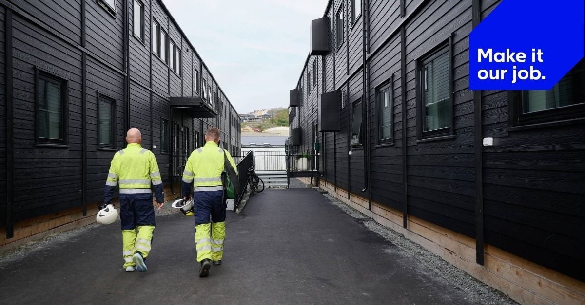 Adapteo-branded image showing two workers in high-visibility clothing walking between black modular accommodation buildings, with the tagline “Make it our job.”